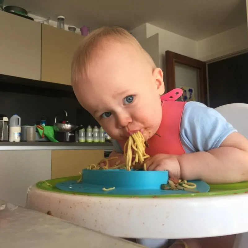 dexter sat on his highchair with lots of noodles coming out of his mouth