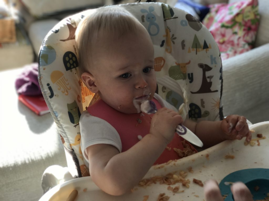 dexter eating yoghurt with a spoon whilst sat in the joie mimzy snacker