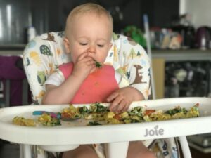 Dex sat on his joie mimzy snacker high chair putting his hand to his mouth