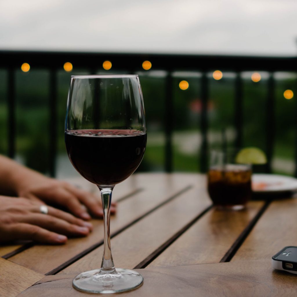 glass of red wine on a wooden table outdoors with fairy lights on the fence