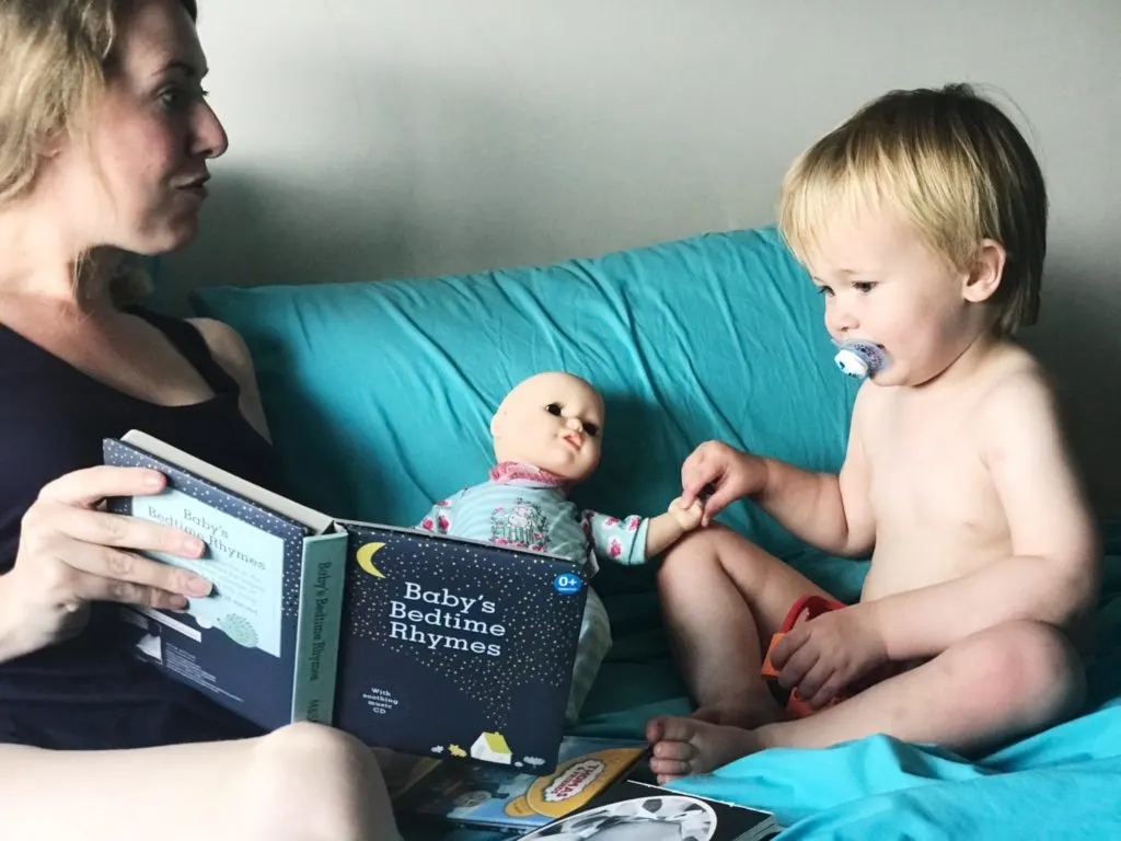 Dexter holding hands with Baby Annabell brother doll while Nicola reads them both a book from baby's bedtime rhymes