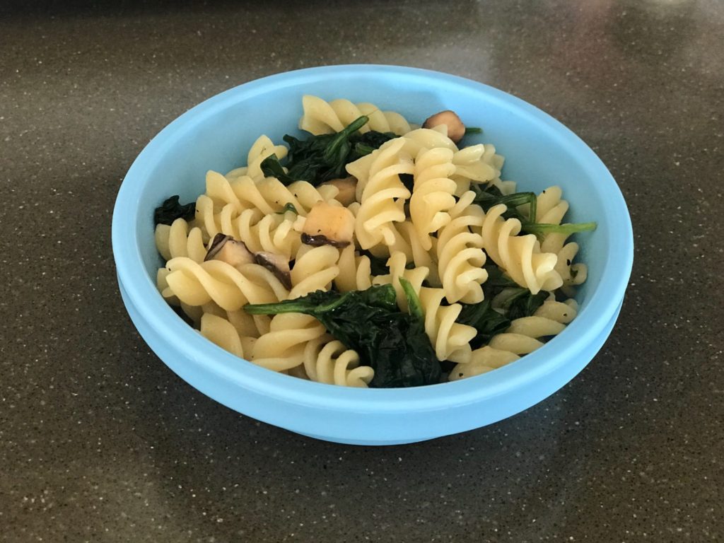 A bowl of spinach and mushroom toddler pasta served in a blue bowl