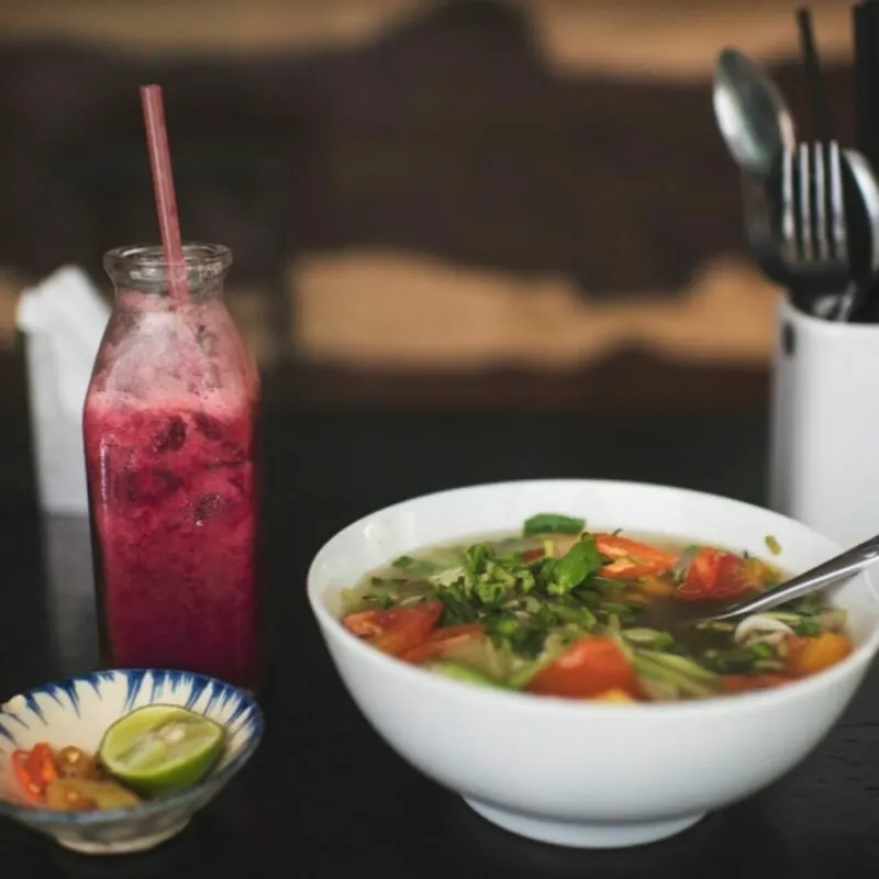 a bowl of vietnamese food along with a pink drink served in a bottle