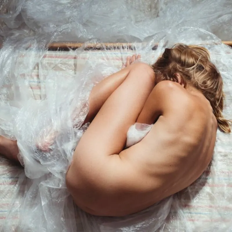 naked woman curled up hanging onto plastic wrap