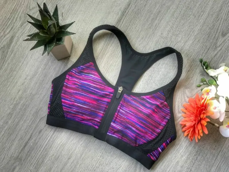 a purple and black zipped front maternity lingerie sport bra flat lay on floor with cactus and orange flower