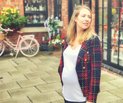 A pregnant woman wearing a red and black jacket, clearly pregnant and looking out into the distance