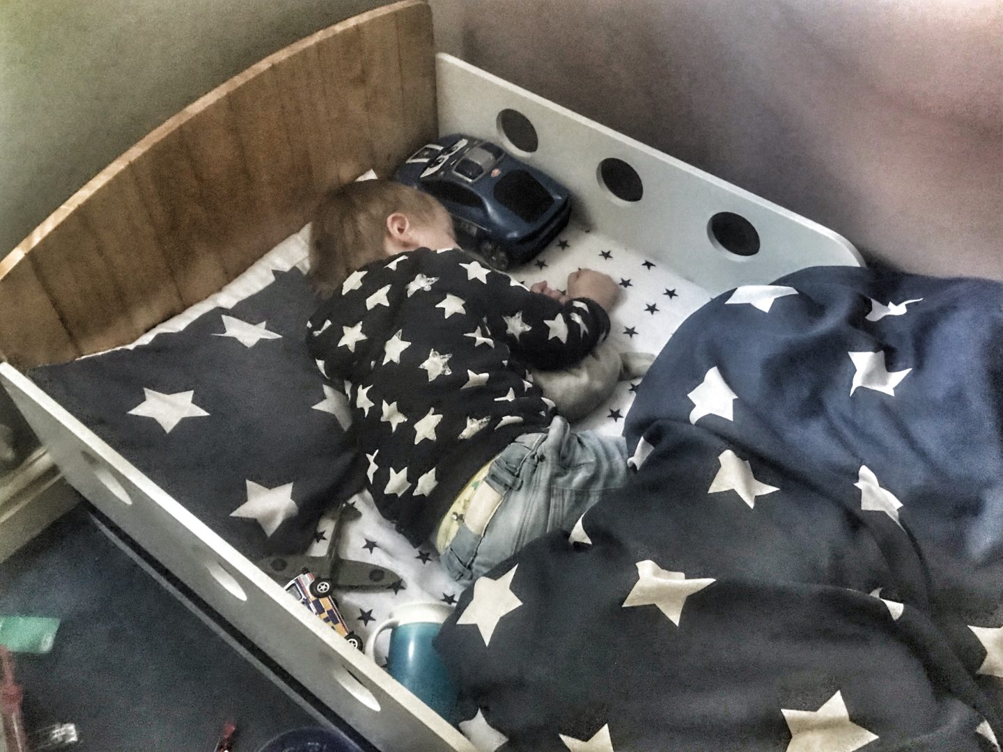 transitioning to a toddler bed, here is Dexter in his toddler bed asleep wearing a navy blue hoodie with white stars and the same style bedding