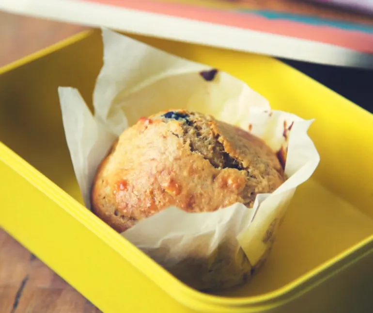 a muffin in a paper case placed in a yellow tupperware bowl