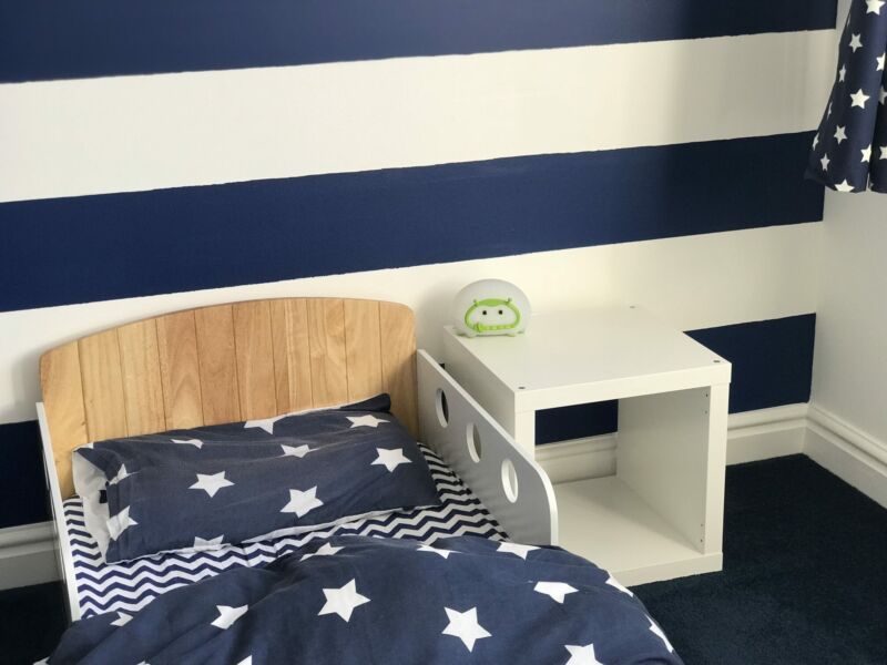 Nautical themed toddler bedroom showing a toddler bed shaped like a boat and a bedisde table with a lumie nightlight on it