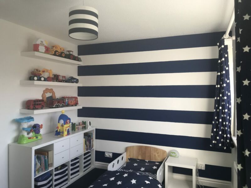 Nautical themed toddler bedroom showing striped navy and white walls, toddler bed, kallax unit and shelves