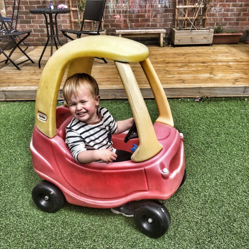 Dexter driving the little tikes cozy coupe on artifical grass outside