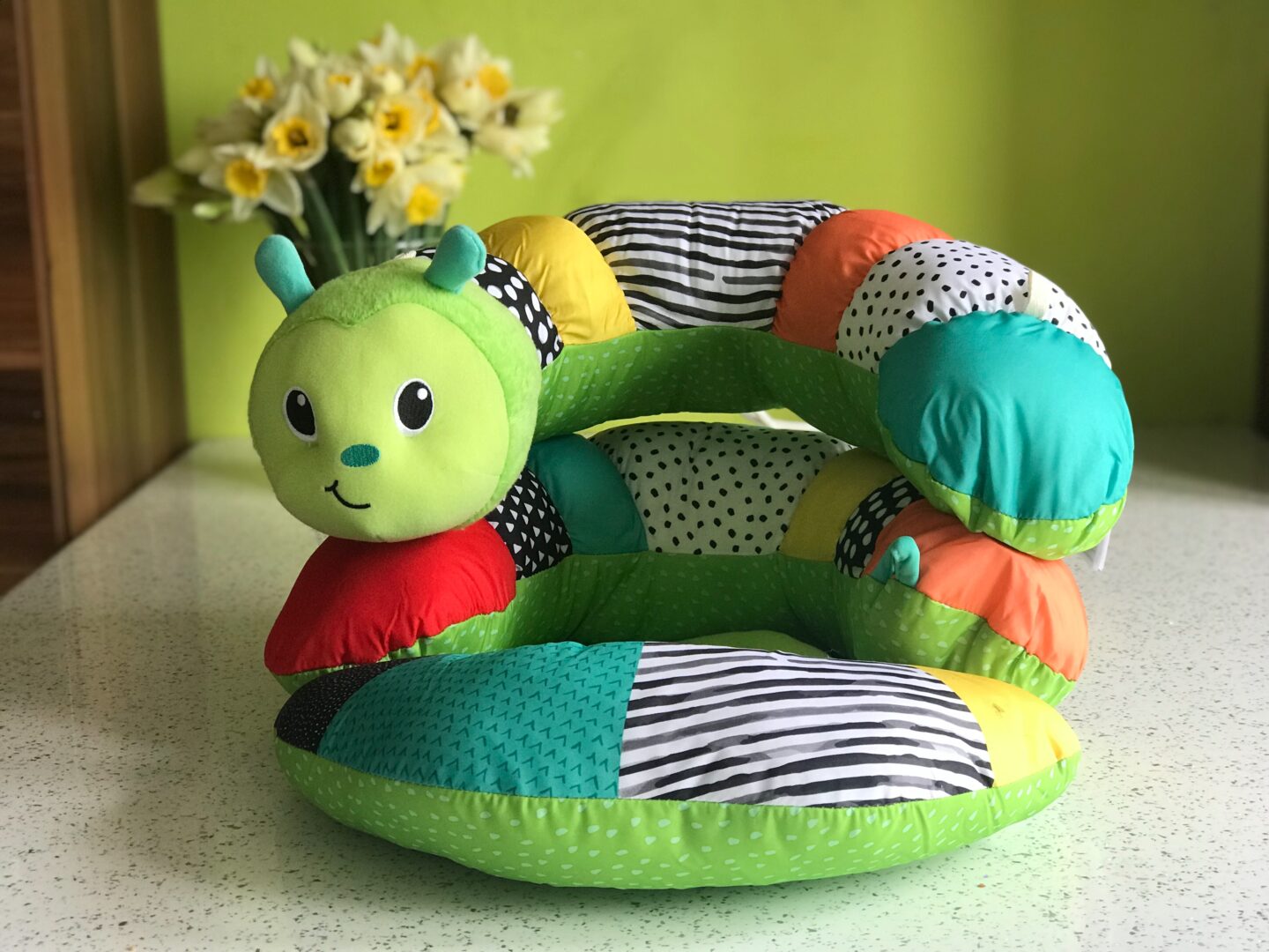 The Infantino Prop-a-Pillar tummy time support stacked so it becomes the seated support. Yellow daffodils in a vase in the background
