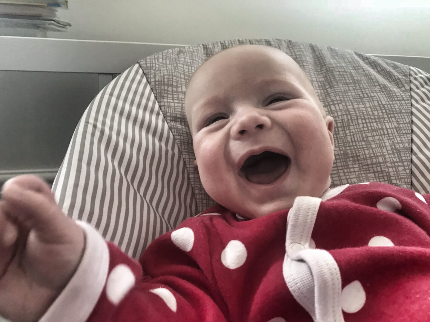 Felix at 11 weeks old wearing a red sleepsuit with white spots smiling