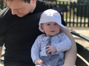 Felix sitting on daddy’s lap in a white sun hat
