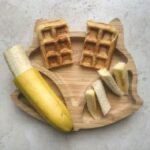 Sweet potato waffles on a bamboo bamboo plate served alongside banana