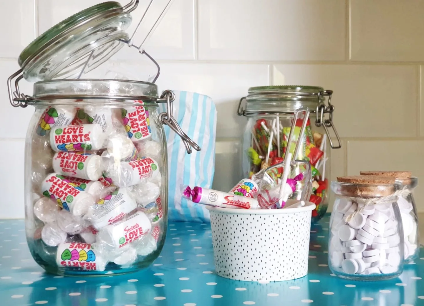 Swizzels Love Hearts in a glass jar next to a tub filled with Swizzels Pick n Mix sweets and a scoop