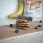 banana, oat and peanut butter pancakes surrounded by blueberries on a chopping board