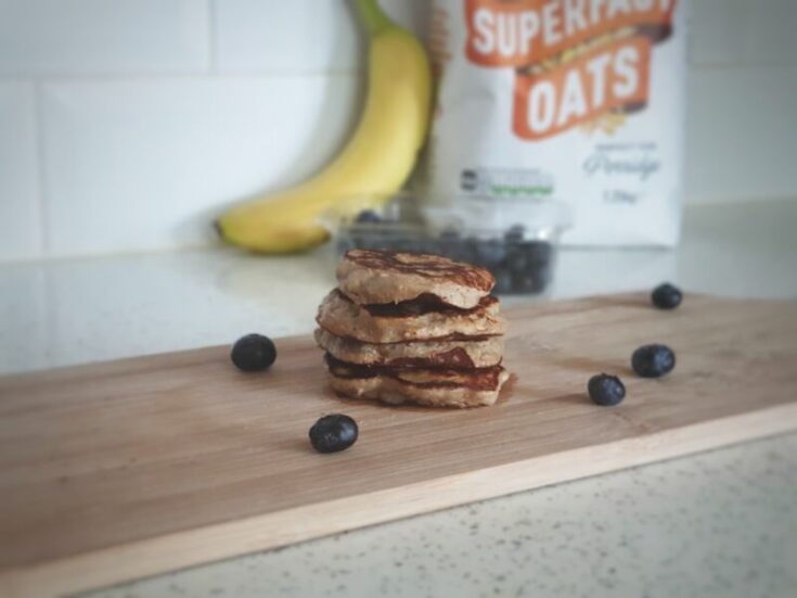 banana, oat and peanut butter pancakes surrounded by blueberries on a chopping board