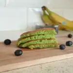 spinach and banana pancakes on a chopping board surrounded by blueberries