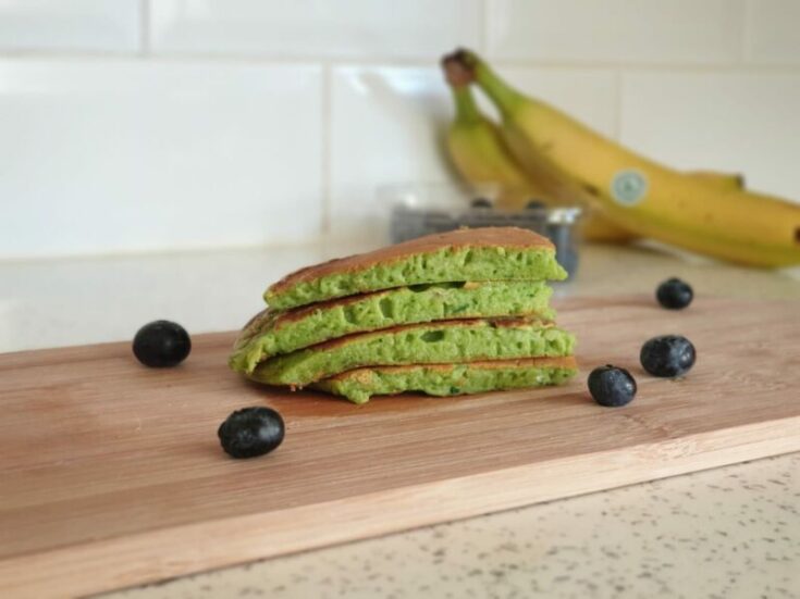 spinach and banana pancakes on a chopping board surrounded by blueberries