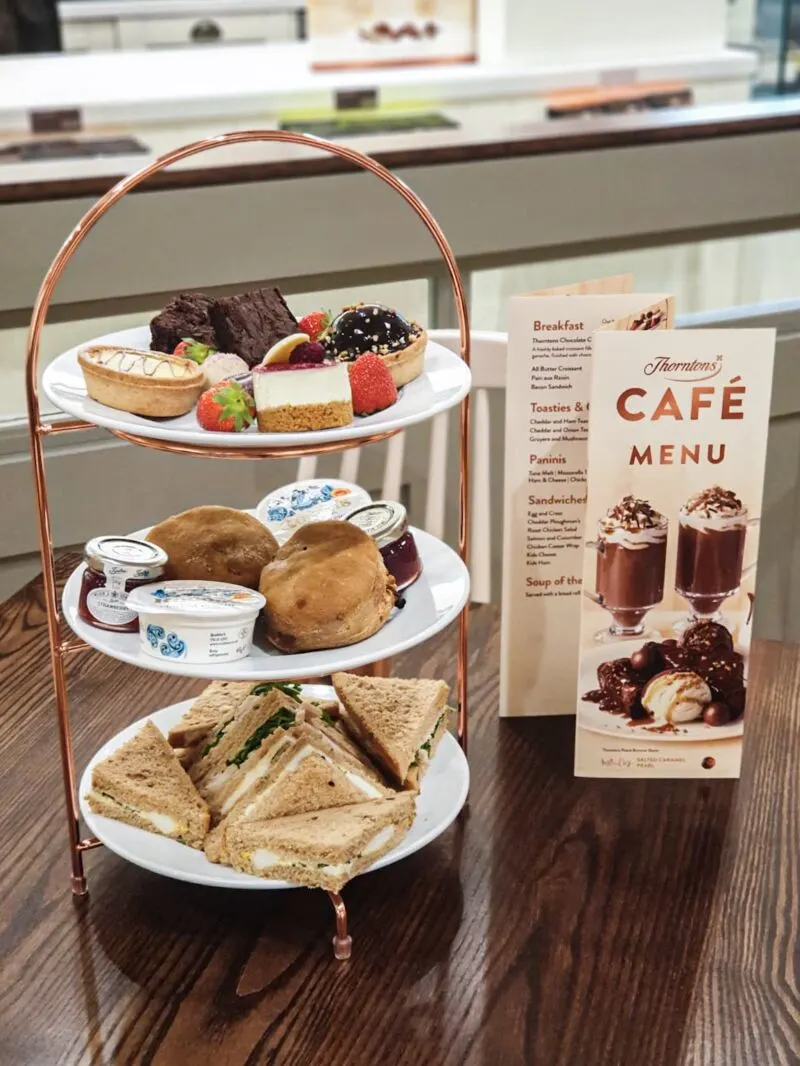 Cake and sandwiches stacked on afternoon tea tray next to a menu in Thornton's new store in Liverpool One