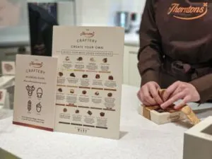 Thornton's employee wrapping our crafted chocolates next to a sign describing each chocolate