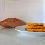 Sweet potato pancakes on a white plate with sweet potatoes in the background