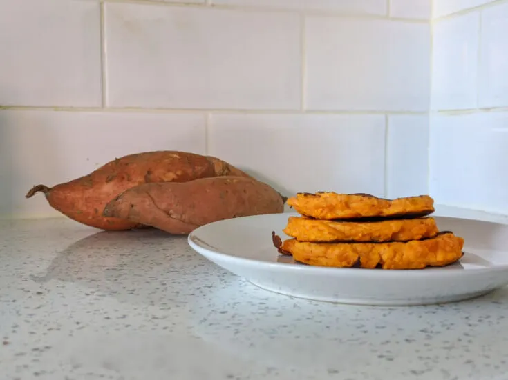 Sweet potato pancakes on a white plate with sweet potatoes in the background