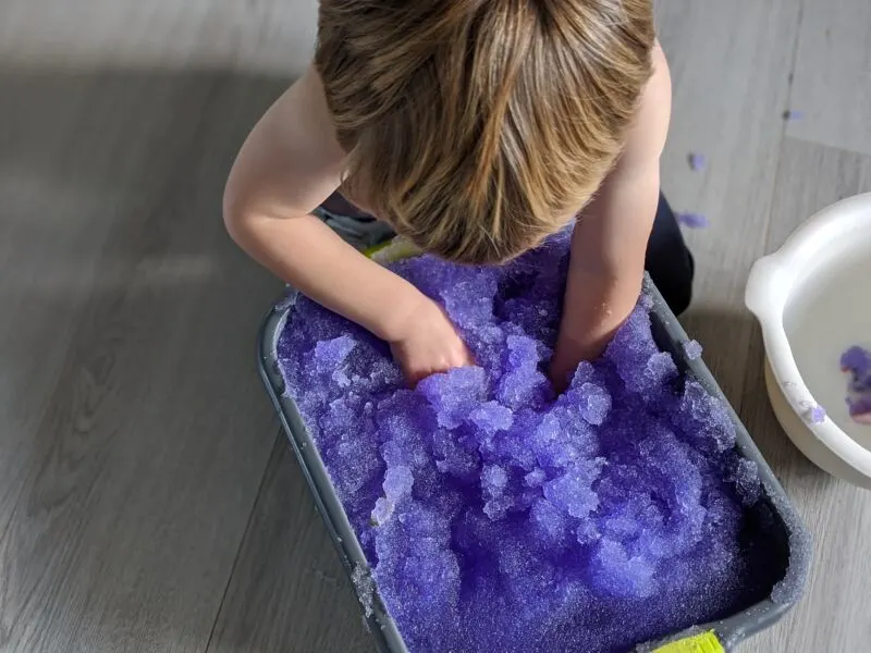 Dexter putting his hands into a washing up bowl full of purple Smelli Gelli Baff