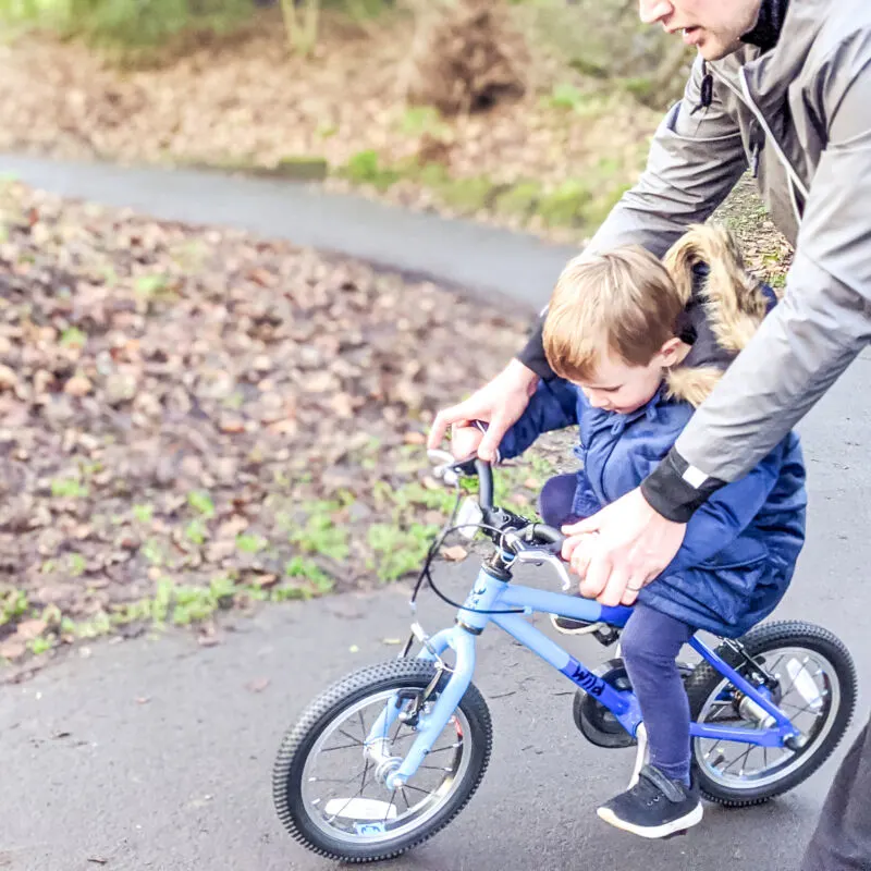 Dexter riding his bike in Hesketh Park whilst being pushed by his dad