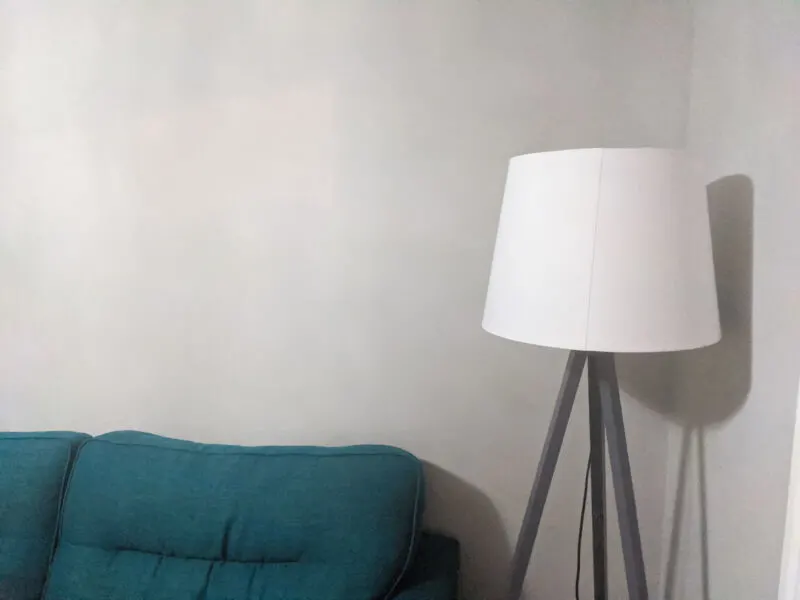 The grey walls of our lounge behind a teal sofa and grey and white lamp