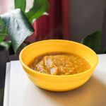 Carrot and coriander soup in a bowl in front of a cheese plant