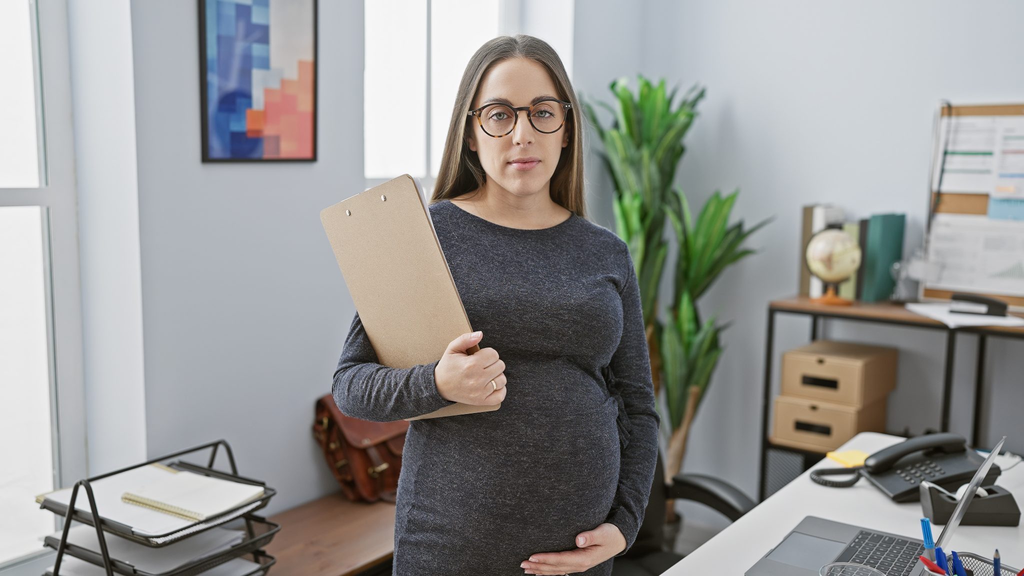 Pregnant hispanic woman posing in office with clipboard, exuding ...